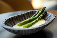 Fresh green asparagus spears served on dark ceramic plate with creamy sauce, shallow depth of field creates elegant restaurant presentation style.