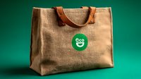 Reusable eco-friendly shopping bag made from natural jute fiber with leather handles and green eco label on emerald background. Sustainable lifestyle concept.