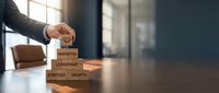 Executive hand stacking wooden blocks with business words for corporate strategy, leadership development, and organizational growth planning concepts.
