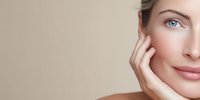 Close-up portrait of woman with flawless skin touching face against neutral beige background, showcasing natural beauty and skincare concept.