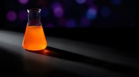 Orange liquid in laboratory flask glowing on dark surface with colorful bokeh lights background for scientific research and chemistry experiments.