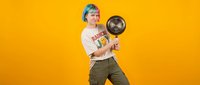 Young Caucasian man with colorful hair holding frying pan on bright yellow background. Cooking concept for kitchen advertising and culinary content.