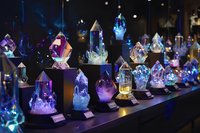 Colorful crystal collection display with amethyst quartz and gemstone specimens on illuminated shelves in dark museum or shop setting for geology education.