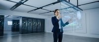 Professional businesswoman presenting data analytics in modern server room with holographic display technology for corporate presentations.