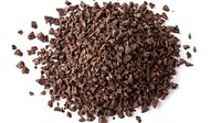 Pile of dark chocolate shavings or cocoa nibs isolated on white background, scattered crumbled pieces for baking and confectionery use.