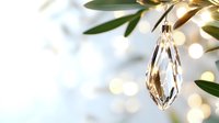 Crystal teardrop ornament hanging from olive branch against soft bokeh background, elegant holiday decor with natural greenery and sparkling light effects.