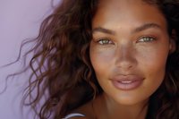 Close up portrait of young mixed race woman with natural curly hair and bright blue eyes against purple background, fresh glowing skin and minimal makeup.