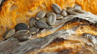 Freshly baked artisan bread loaf with pumpkin seeds scattered on rustic wooden surface. Homemade bakery product with golden crust for healthy eating concepts.