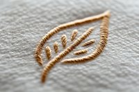 Golden leaf embroidery detail on white linen fabric showcases delicate needlework craftsmanship with metallic thread creating elegant botanical motif.