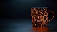 Coffee mug with electronic circuit board pattern glowing in orange light on dark background for technology and programming themes.