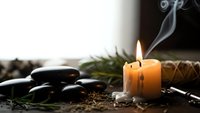 Spa wellness scene with burning candle, hot stones, and aromatic herbs creating peaceful atmosphere for relaxation and meditation therapy.
