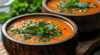 Creamy orange soup garnished with fresh herbs and black sesame seeds served in rustic wooden bowls. Traditional homemade vegetarian appetizer with vibrant colors.