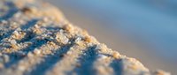 Macro close-up of frost crystals forming on a textured surface with warm golden sunlight and cool blue shadows, suitable for winter backgrounds and seasonal designs.