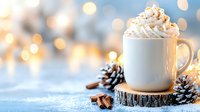 Hot chocolate topped with whipped cream in white mug on wooden coaster, surrounded by pine cones and winter decorations against blurred bokeh lights background.