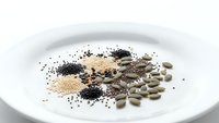 Assorted superfood seeds and grains on white plate including chia, quinoa, pumpkin seeds for healthy nutrition and wellness recipes.