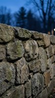 Ancient weathered stone wall with moss-covered rocks stacked in traditional masonry construction against blurred winter landscape background.