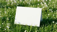 Blank white card mockup on green grass with small white flowers for spring marketing materials and outdoor advertising campaigns.