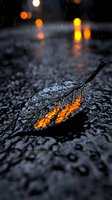 Fallen autumn leaf on wet asphalt reflecting orange street lights during rain, with bokeh effects and water drops creating moody atmospheric night scene.