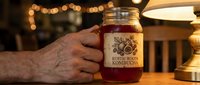 Hand holding glass jar of fermented kombucha tea with rustic label in warm kitchen setting with bokeh lights creating cozy atmosphere for healthy lifestyle.