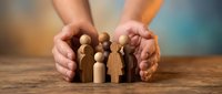 Protective hands surrounding wooden family figures on table representing insurance, care, safety and security concepts for business presentations.