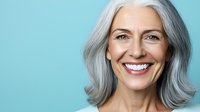 Confident mature Caucasian woman with natural gray hair and bright smile against turquoise background showing positive aging and wellness concept.