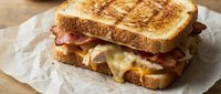 Grilled cheese sandwich with crispy bacon and melted cheese on toasted bread served on parchment paper for comfort food and breakfast menu concepts.