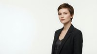 Professional businesswoman in black suit jacket with short brown hair on neutral background for corporate presentations and marketing materials.