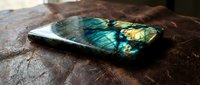 Polished labradorite gemstone slab displaying vibrant blue and green flash colors on rustic wooden surface for jewelry making and crystal healing practices.