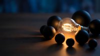 Glowing incandescent bulb surrounded by dark spheres on surface, representing innovation, creativity, and unique ideas for business and technology concepts.
