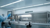 Pharmaceutical manufacturing facility with sterile production line and technician in protective suit operating automated filling equipment in cleanroom environment.
