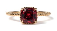 Elegant gold ring with deep red cushion-cut gemstone, featuring intricate beaded band design for engagement or special occasion jewelry.