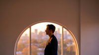 Young professional man silhouette standing by large round window overlooking city skyline at sunset, contemplating future opportunities and success.