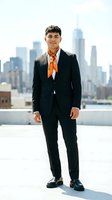 Young Asian businessman in black suit with orange tie standing confidently on rooftop terrace with city skyline background for corporate marketing materials.