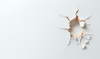 Hole with cracked edges in white wall or paper surface, creating dramatic breakthrough effect for design projects.