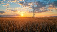 High voltage power line tower stands in golden wheat field at dramatic sunset with orange clouds and blue sky, rural landscape with electricity pylon.