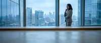 Professional businesswoman in suit standing by floor-to-ceiling windows overlooking modern city skyline, contemplating future opportunities in corporate office.