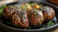 Juicy herb-crusted meatballs sizzling in cast iron skillet with fresh parsley garnish, perfect for restaurant menus and home cooking content.