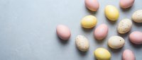 Pastel Easter eggs in pink, yellow, and cream tones scattered on a light gray stone surface, flat lay with copy space for spring holiday designs.