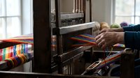 Skilled artisan weaving colorful threads on traditional wooden loom in bright workshop, showcasing ancient textile craftsmanship and handmade fabric creation.