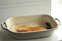Dirty white ceramic baking dish with burnt food residue and grease stains after cooking, showing wear and use in kitchen. Needs cleaning.