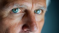Close up portrait of mature Caucasian man with intense blue eyes and wrinkled skin in dramatic lighting, showing wisdom and life experience against dark background.