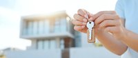 Hands holding house keys with modern residential building in background, real estate purchase, new home ownership, property investment concept.