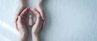 Hands forming protective circle around wooden house model on white background symbolizing home insurance and real estate protection concept.