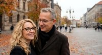 Happy mature couple walking together in autumn city square enjoying romantic date outdoors with colorful fall foliage and historic architecture background.