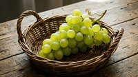 Fresh green grapes in woven basket on rustic wooden table, ideal for food, agriculture, harvest, and culinary content.