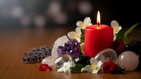 Red candle burning surrounded by healing crystals, white orchid flowers and lavender creating peaceful spa meditation atmosphere for wellness rituals.