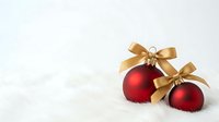Red matte ornaments with gold ribbon bows nestled in snow, perfect for holiday and festive season marketing materials.