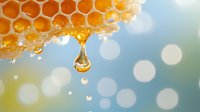 Fresh honey drips from natural honeycomb with golden droplet suspended in mid-air against soft bokeh background, capturing sweet organic food moment.