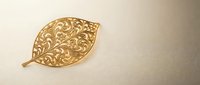 Ornate golden leaf with intricate filigree pattern and decorative swirls on neutral background for luxury design projects and elegant branding materials.