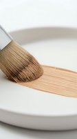 Paintbrush with natural bristles applying white paint or coating onto ceramic bowl, isolated on white background for design and craft projects.
